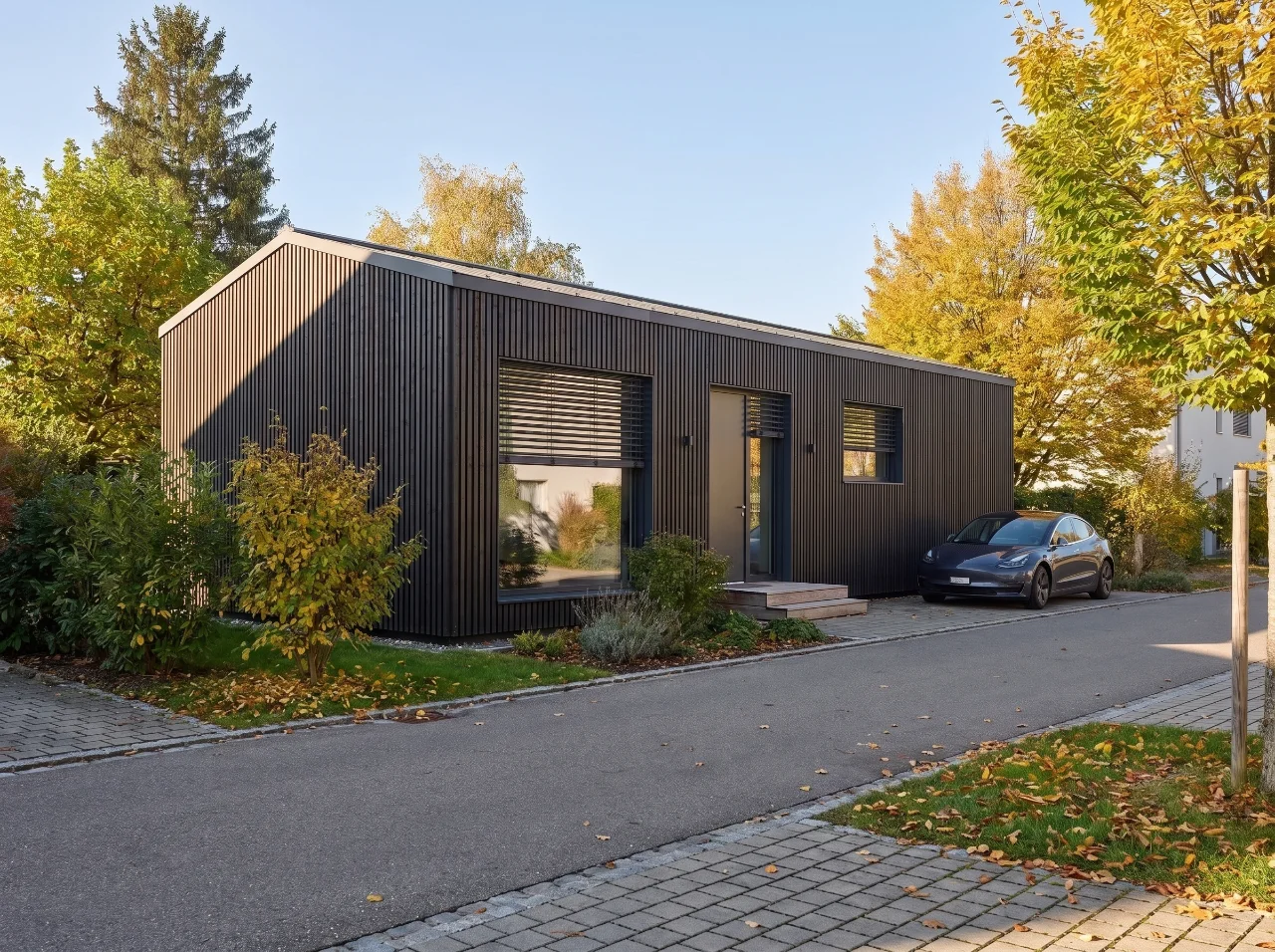 Bungalow S with gable roof: view from the street with vertical timber cladding and driveway in autumn